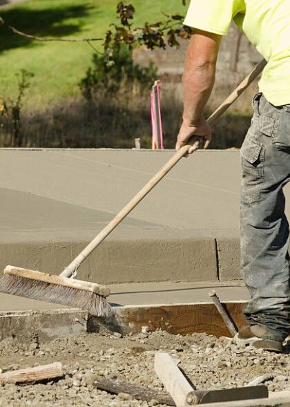 Concrete construction contractor using a broom to install texture in a sidewalk, curb and storm drainage gutter on a new urban road street project